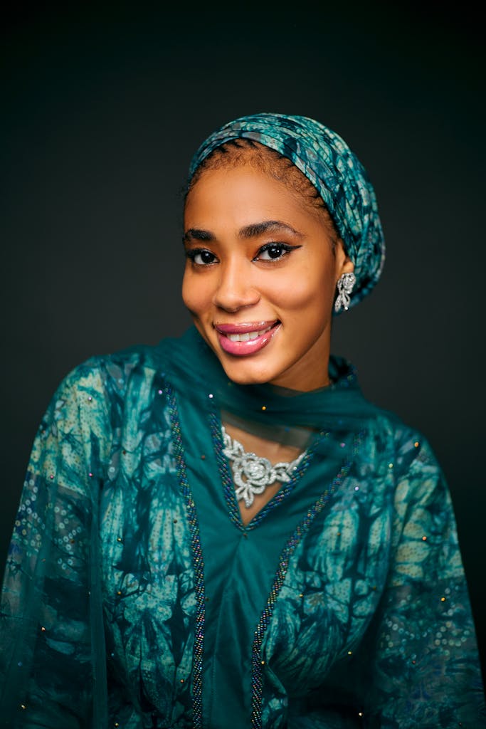 A woman in traditional green attire smiles warmly against a dark backdrop.