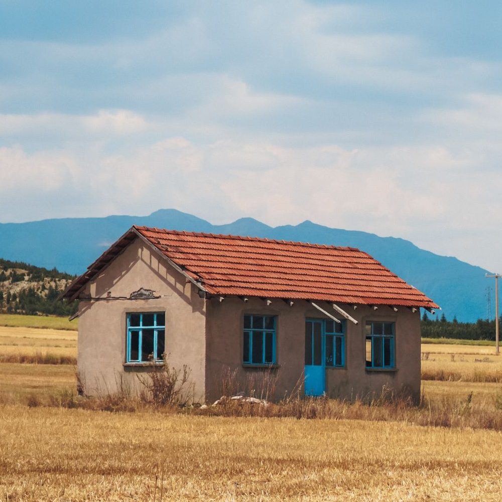 Scenic view of old building facade on meadow against mounts under sky with fluffy clouds in countryside